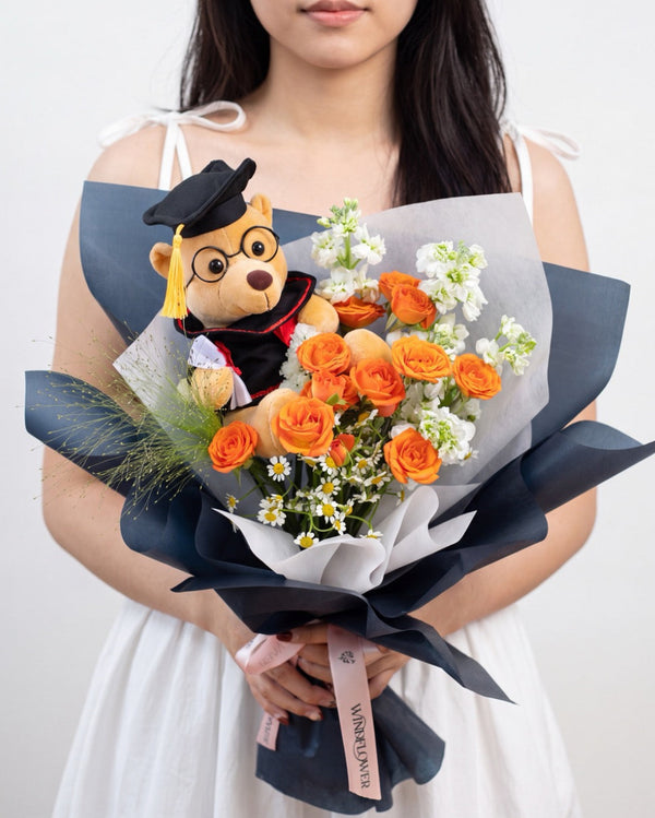 Atelier Amber — graduation bear with orange roses and white stock flowers wrapped in navy paper, held by a model