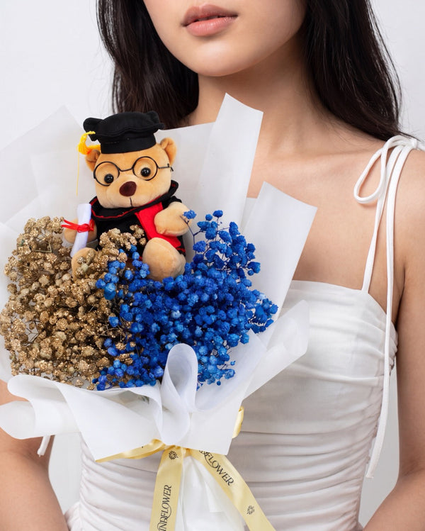Laureate in Gilded — graduation bear with gold and blue baby's breath wrapped in white paper, held by a model