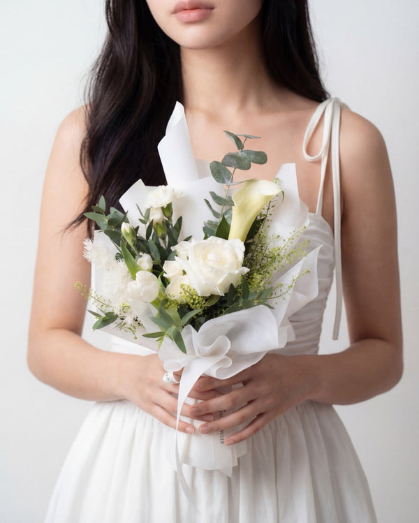 Infinity Love In White — white roses and a calla lily with eucalyptus, wrapped in white paper, held by a model