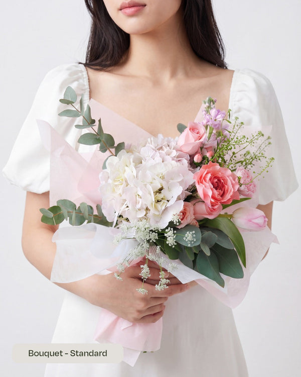 Haru — pink hydrangea, pink roses and pastel blooms with greenery, wrapped in sheer paper, held by a model