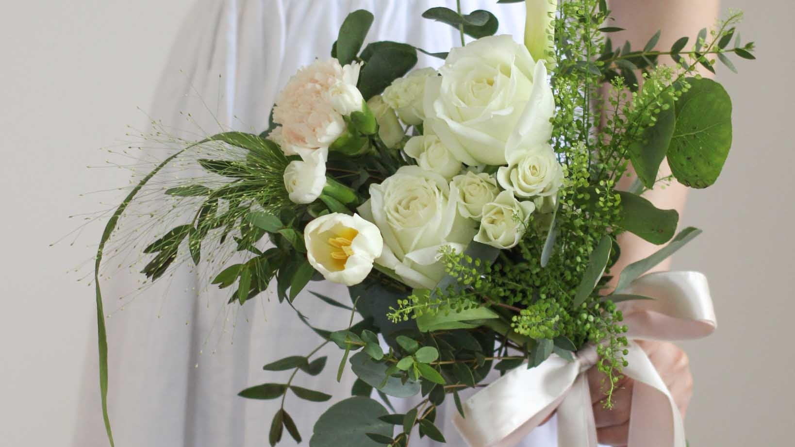 Bride in a white dress holding a bouquet of white roses, tulip and calla lily with trailing greenery