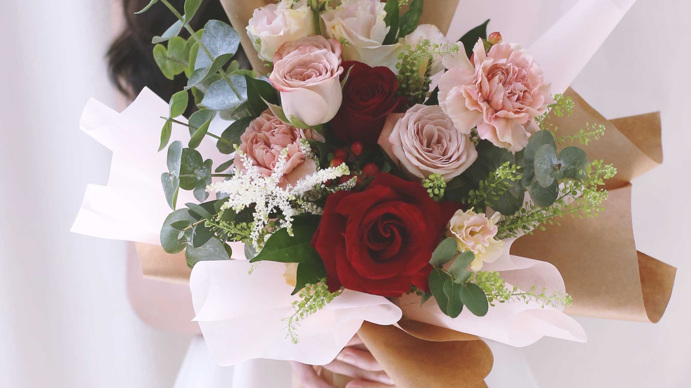 Hand-tied bouquet of cappuccino roses, red roses, carnations and eucalyptus in kraft wrapping
