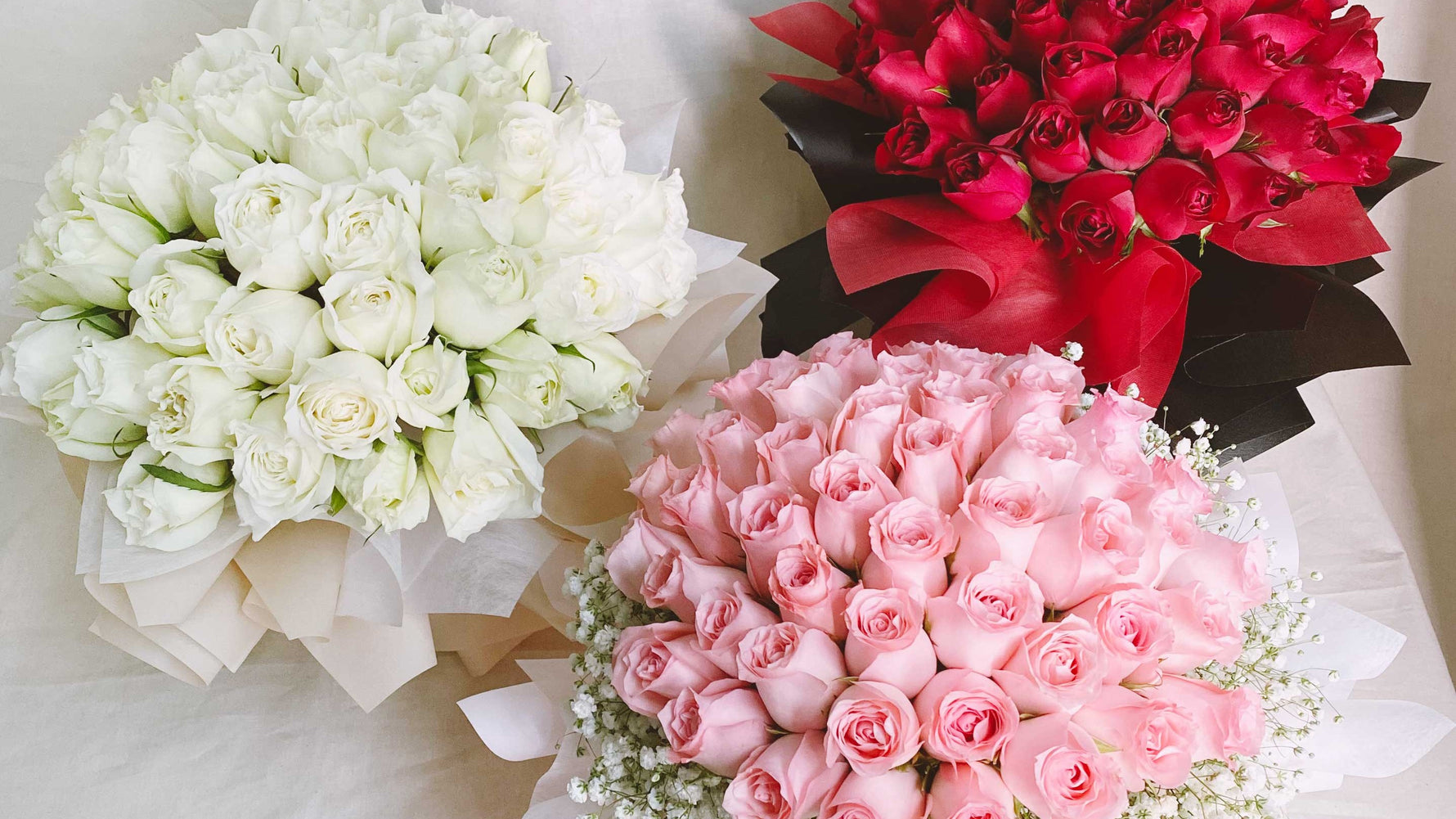 Three 50-stalk rose bouquets in white, red and pink wrapping laid on a cream cloth