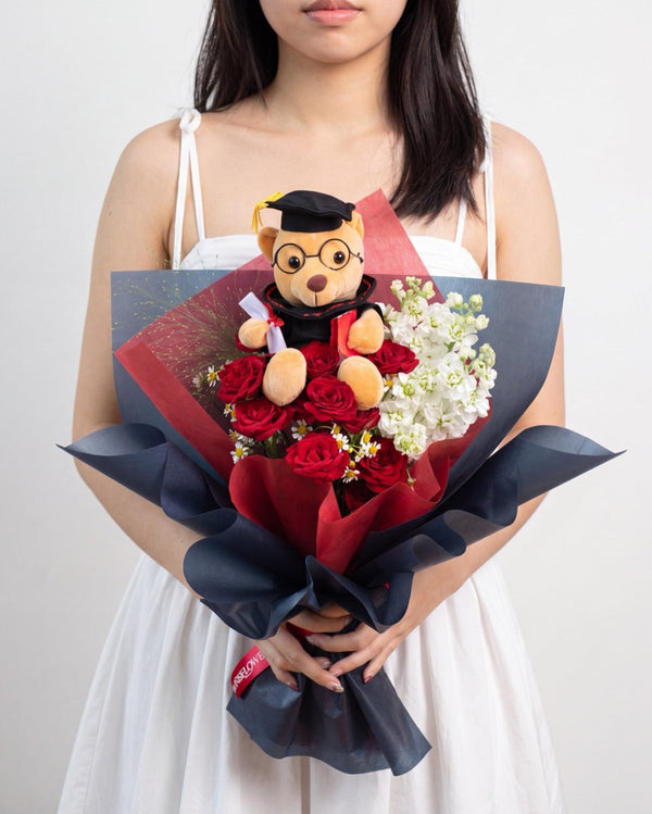 Atelier Rouge — graduation bear with red roses and white stock flowers wrapped in navy and red paper, held by a model