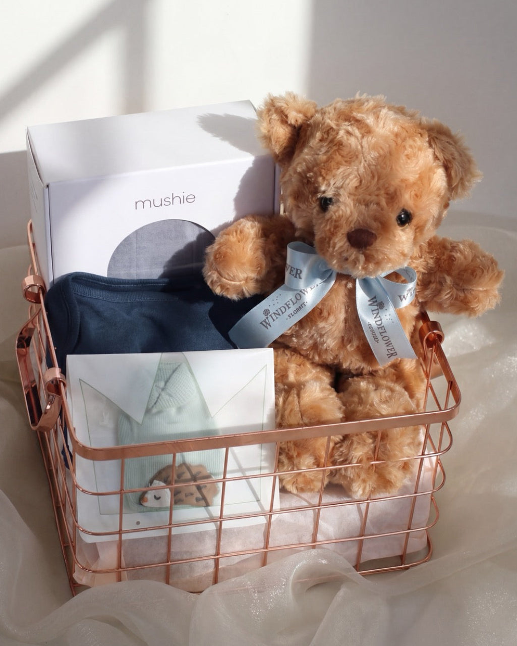 Baby hamper Singapore with Mushie swaddle, bodysuit, booties and Windflower teddy bear in a rose-gold wire basket