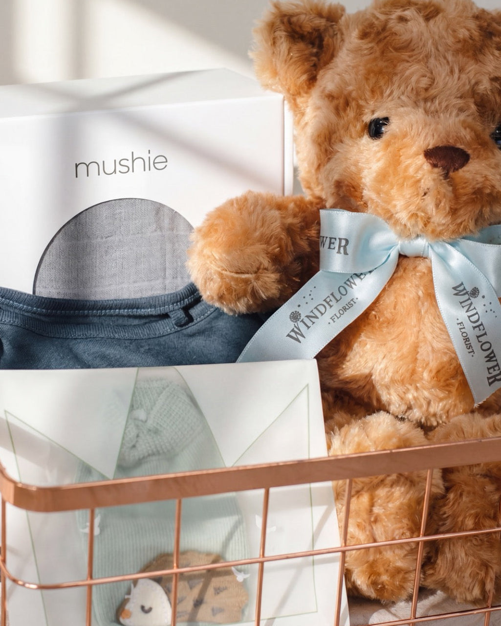 Close-up of baby hamper Singapore with Mushie swaddle box, navy bodysuit and plush teddy bear