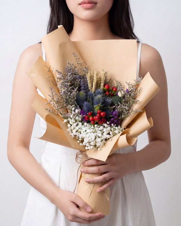 Eryngium Blooms — dried lavender, wheat stalks and blue thistle with red berries, kraft paper wrap, held by a model
