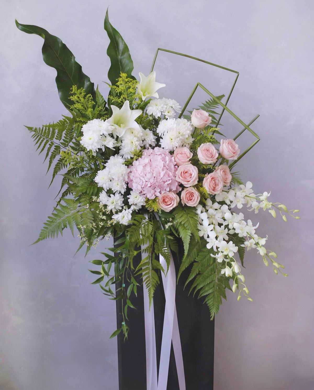 Standing funeral flower arrangement of pink hydrangea, roses, white chrysanthemums and orchids.