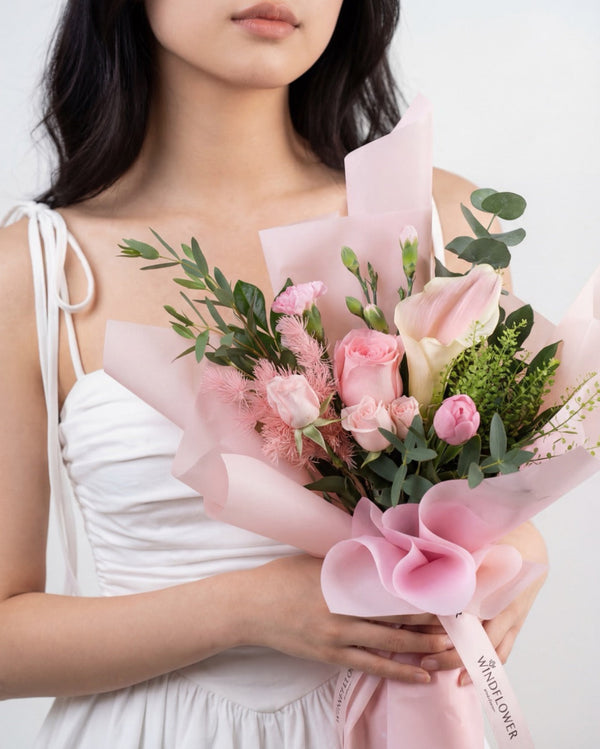 Infinity Love In Pink — pink roses and spray roses with a cream bloom and eucalyptus, wrapped in pink paper, held by a model