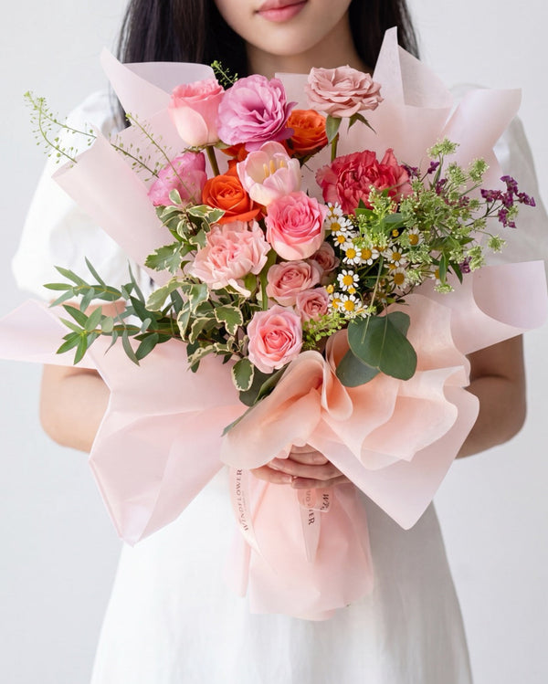Smitten Surprise — pink roses, orange tulips and daisies with pink carnations, pink paper wrap, held by a model