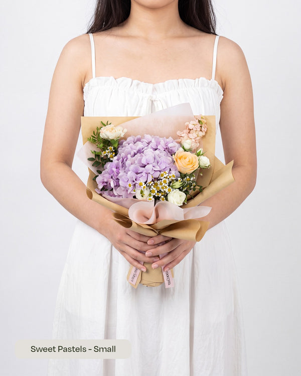 Daily Surprise Fresh Hydrangea — purple hydrangea with peach blossoms and white roses wrapped in kraft paper, held by a model