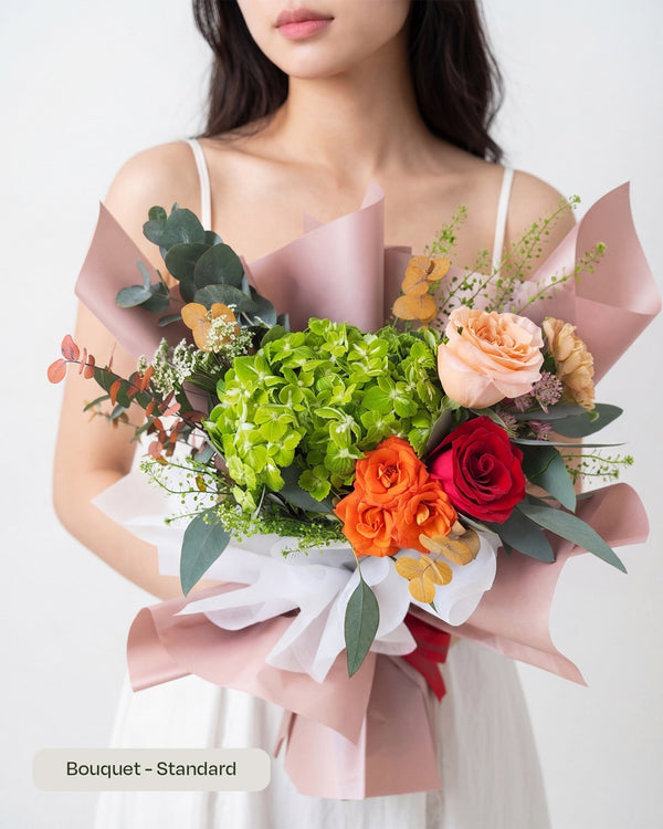 Aki — green hydrangea, orange spray roses and a red rose in pink and white wrap, held by a model.